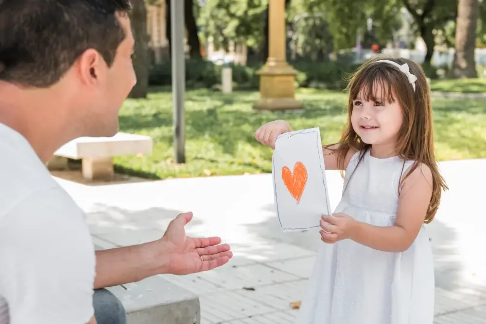 A little girl proudly showing a drawing of a red heart