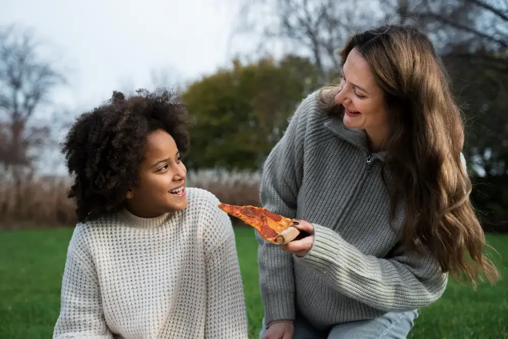 A woman sharing pizza with a smiling child outdoors